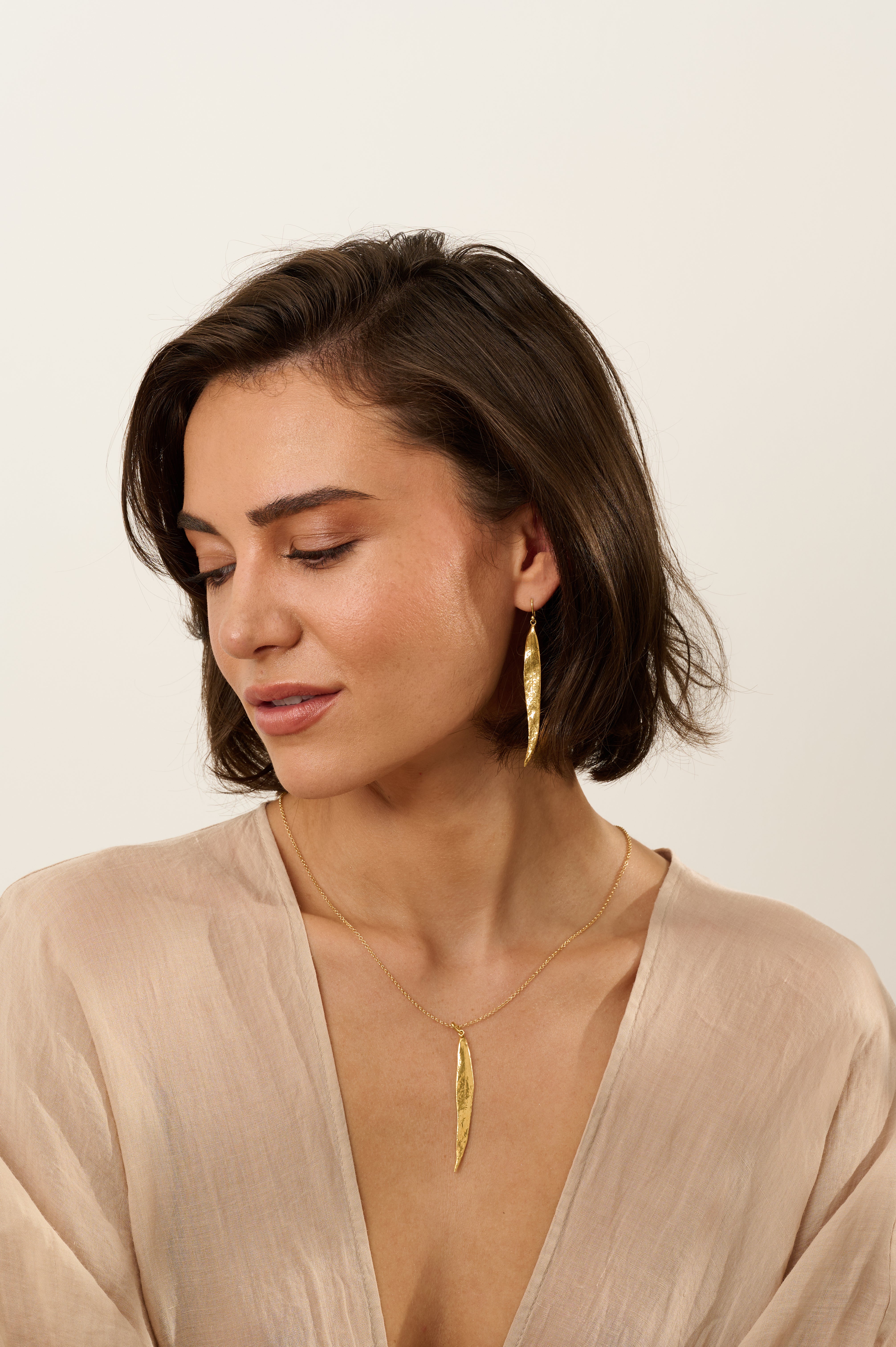 Model wearing matching gold willow leaf necklace and long gold willow leaf earrings, handcrafted botanical jewellery with organic textured leaf design.