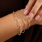 Model wearing layered Iris & Lolli recycled silver bracelets including fine satellite chain and paperclip chains