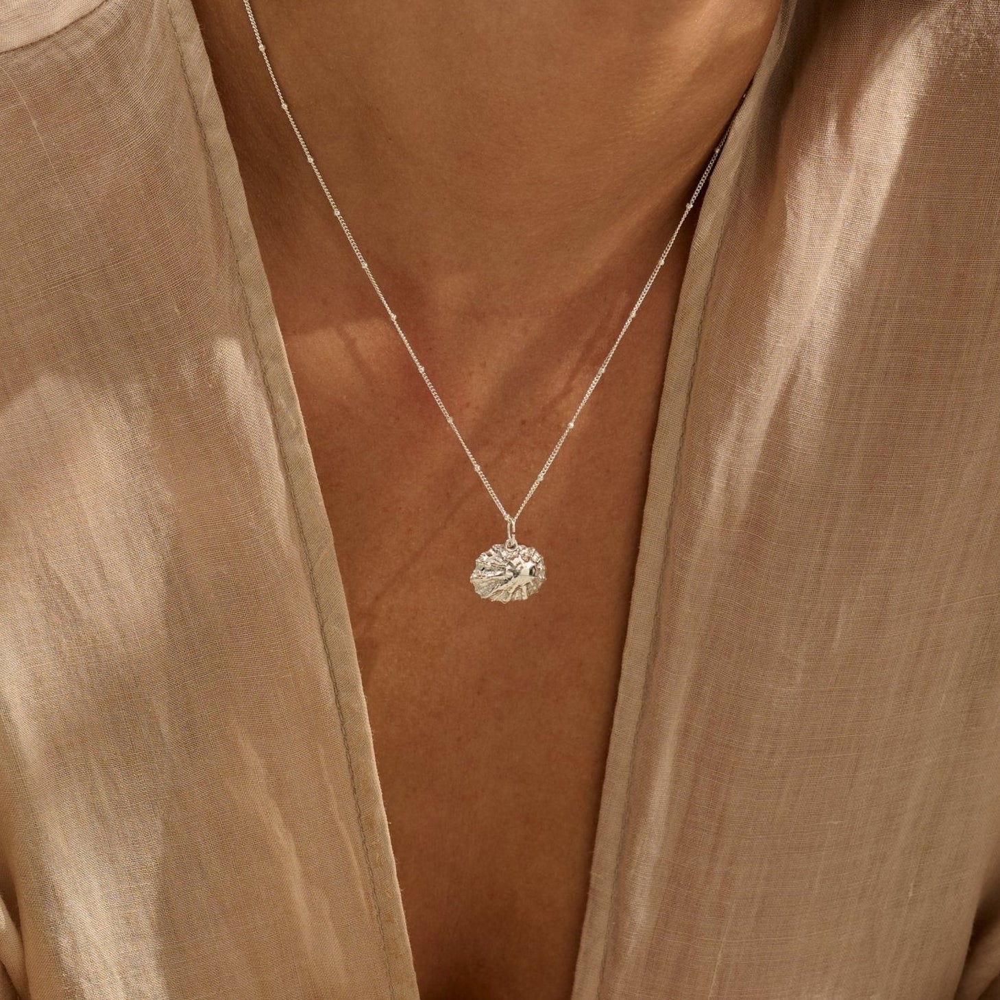 woman wearing fine silver limpet shell pendant necklace, handcrafted coastal inspired jewellery styled with natural linen blouse