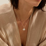 woman wearing fine silver limpet shell pendant necklace, handcrafted coastal inspired jewellery styled with natural linen blouse