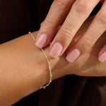 Close-up of a hand wearing a delicate silver satellite bracelet with a blurred background