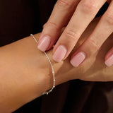 Close-up of a hand wearing a delicate silver satellite bracelet with a blurred background