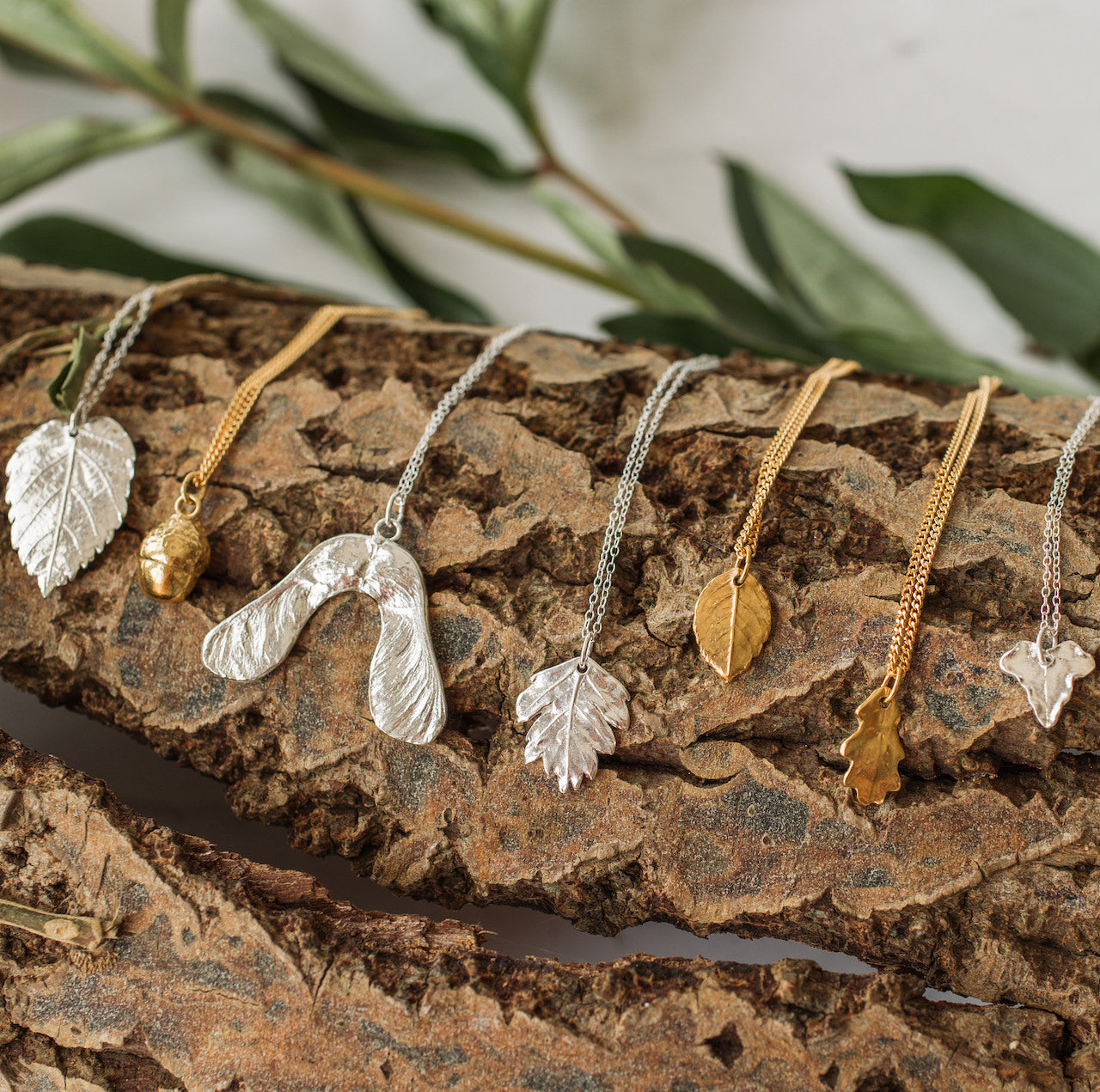 Woodland leaf and seed jewellery displayed on natural bark