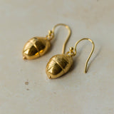 Handmade recycled gold Acorn earrings by Iris and Lolli resting on a soft neutral surface, showing their organic woodland texture and natural golden sheen