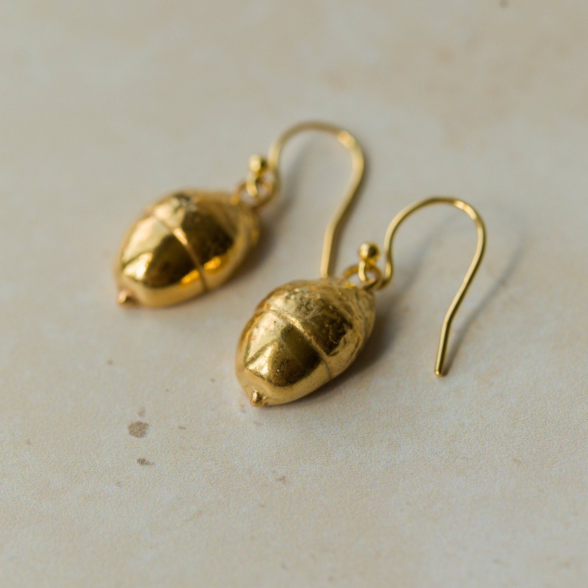 Handmade recycled gold Acorn earrings by Iris and Lolli resting on a soft neutral surface, showing their organic woodland texture and natural golden sheen