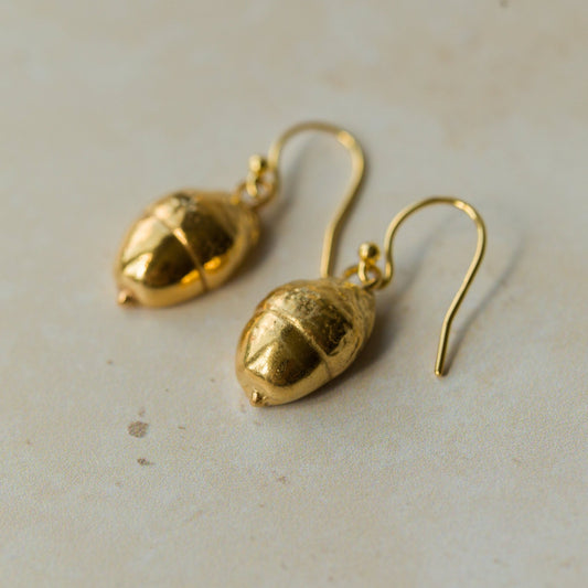 Handmade recycled gold Acorn earrings by Iris and Lolli resting on a soft neutral surface, showing their organic woodland texture and natural golden sheen