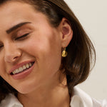 Model wearing handmade recycled gold Venus clam shell drop earrings by Iris and Lolli, ocean inspired and crafted in the UK