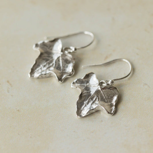 Close-up of handmade recycled silver Ivy Leaf earrings by Iris and Lolli on a soft neutral surface, highlighting the natural leaf texture and organic botanical shape