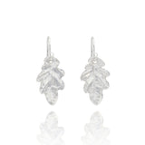 Handmade recycled silver small oak leaf drop earrings by Iris and Lolli on white background, nature inspired and crafted in the UK