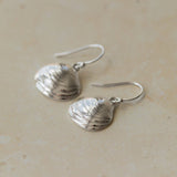 Close-up of handmade recycled silver Shell earrings by Iris and Lolli on a neutral background, showing delicate clam shell texture and natural ocean-inspired detail