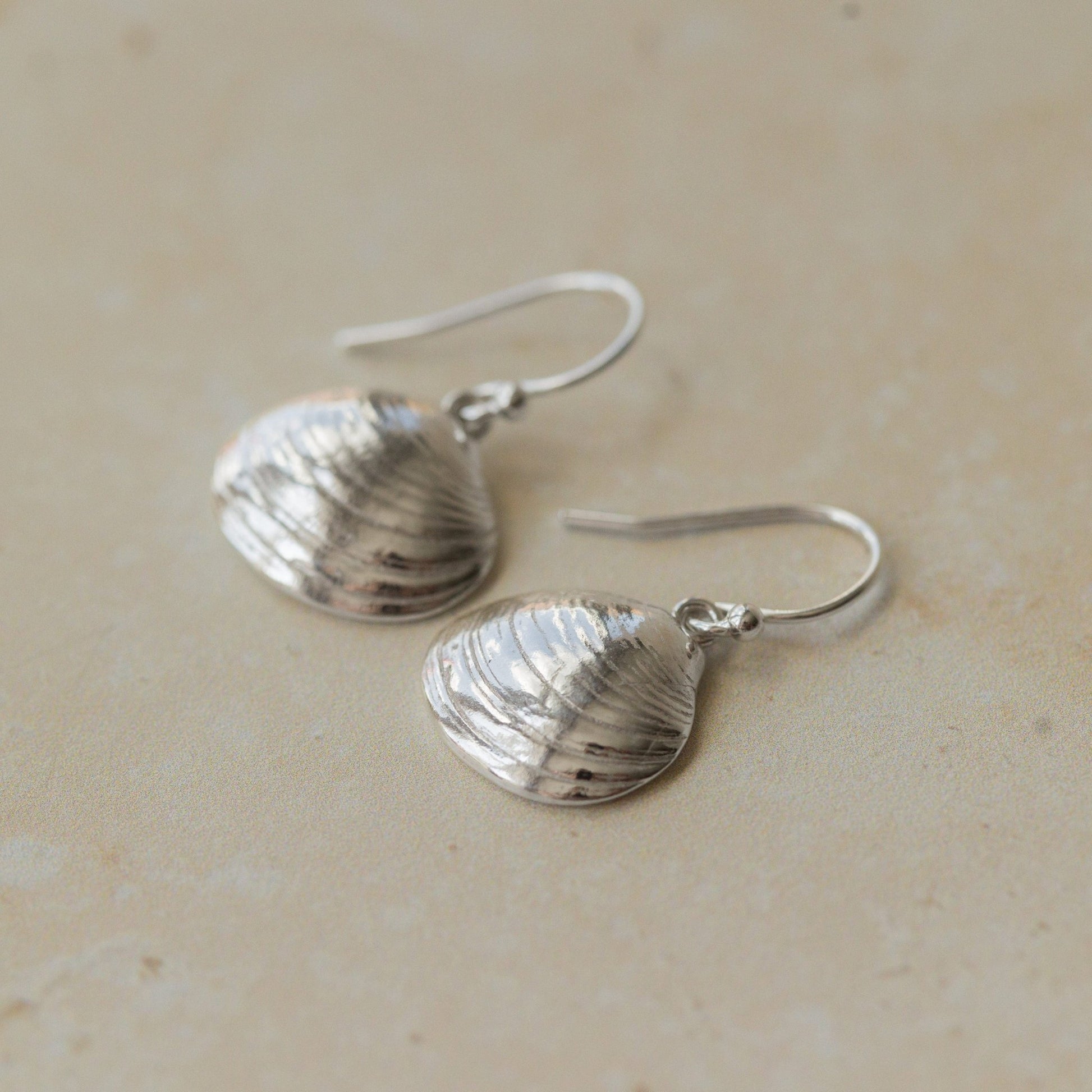 Close-up of handmade recycled silver Shell earrings by Iris and Lolli on a neutral background, showing delicate clam shell texture and natural ocean-inspired detail
