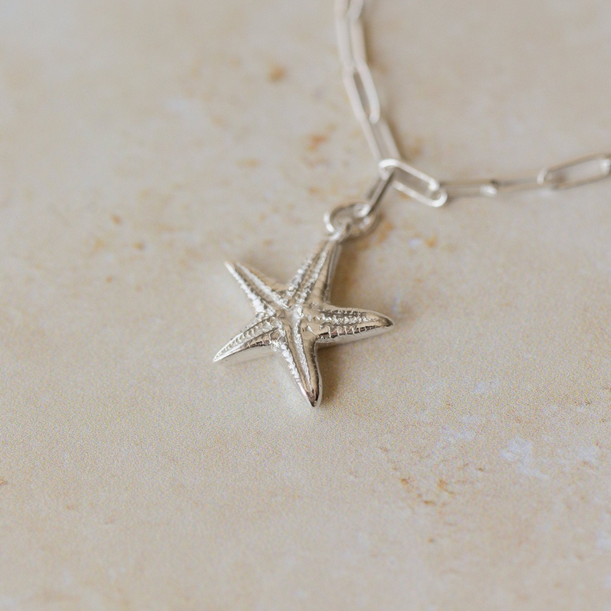 recycled silver starfish charm bracelet with paperclip chain photographed close-up on stone surface, handcrafted coastal jewellery by Iris & Lolli