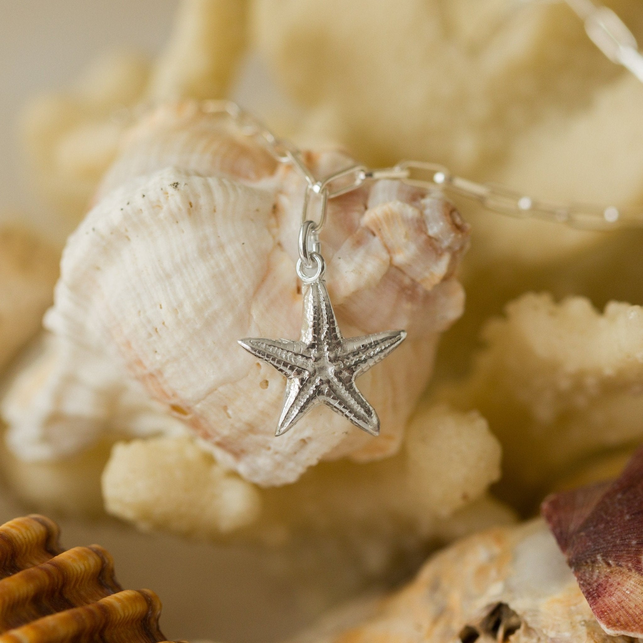 recycled silver starfish charm bracelet resting on natural seashells, handcrafted coastal-inspired jewellery by Iris & Lolli