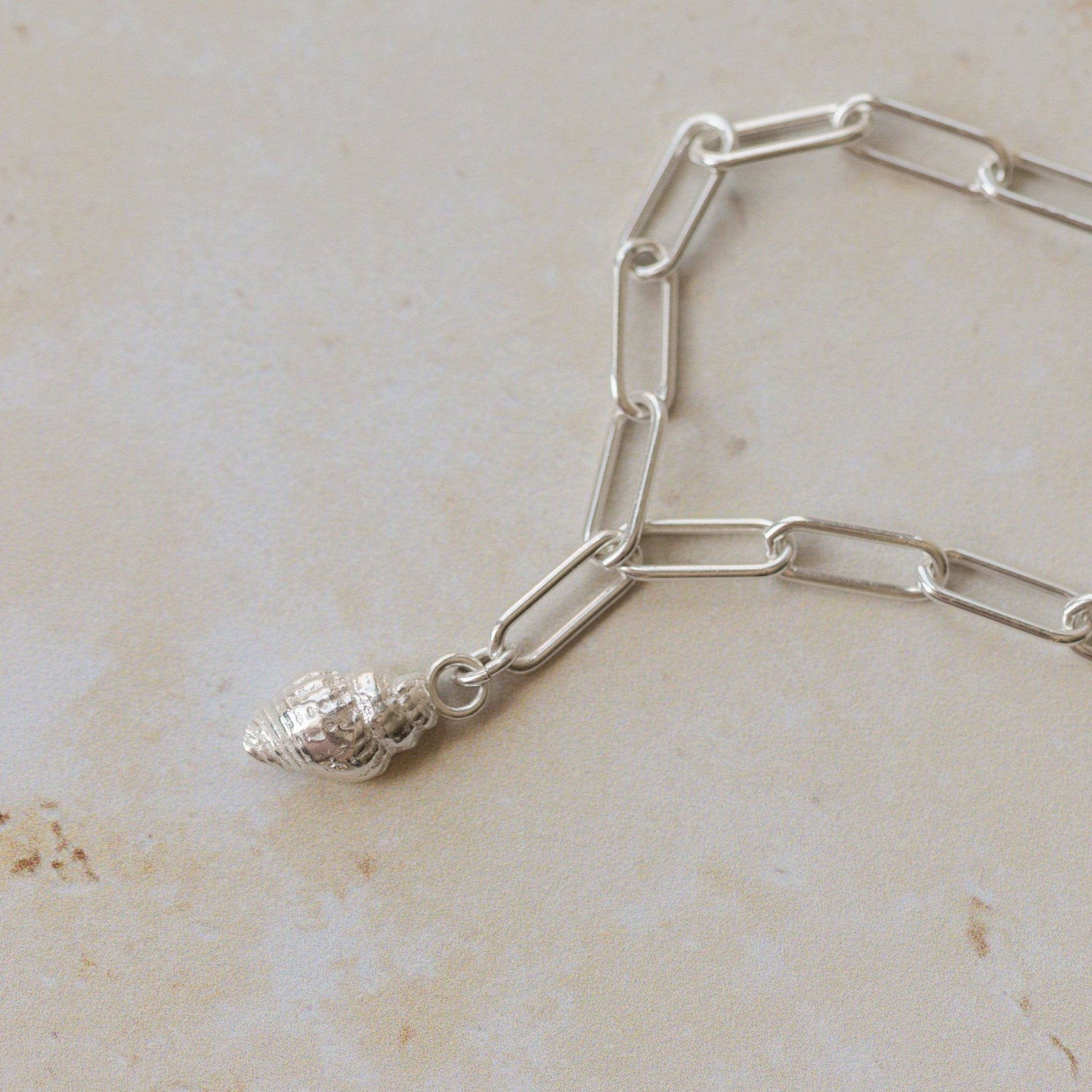 close up of recycled silver whelk shell charm on paperclip chain bracelet, handcrafted coastal design by Iris & Lolli