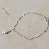 recycled silver whelk shell charm bracelet with delicate paperclip chain displayed on neutral stone background by Iris & Lolli