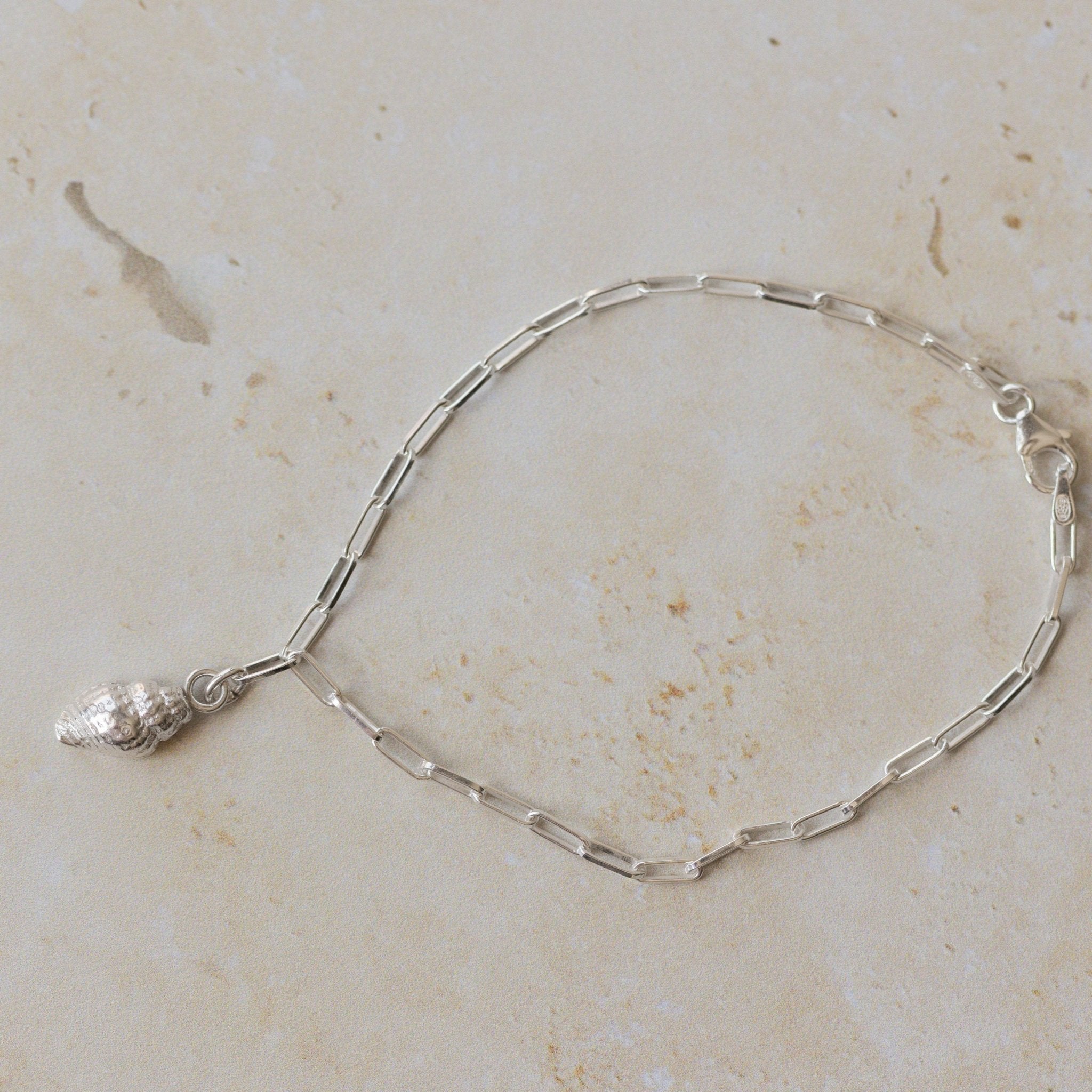 recycled silver whelk shell charm bracelet with delicate paperclip chain displayed on neutral stone background by Iris & Lolli