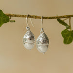 Handmade recycled silver Acorn earrings by Iris and Lolli hanging from a branch with ivy leaves, showcasing their natural woodland texture and polished silver shine