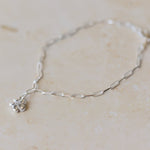 silver forget me not charm bracelet with paperclip chain styled flat on neutral background, delicate floral jewellery by Iris & Lolli