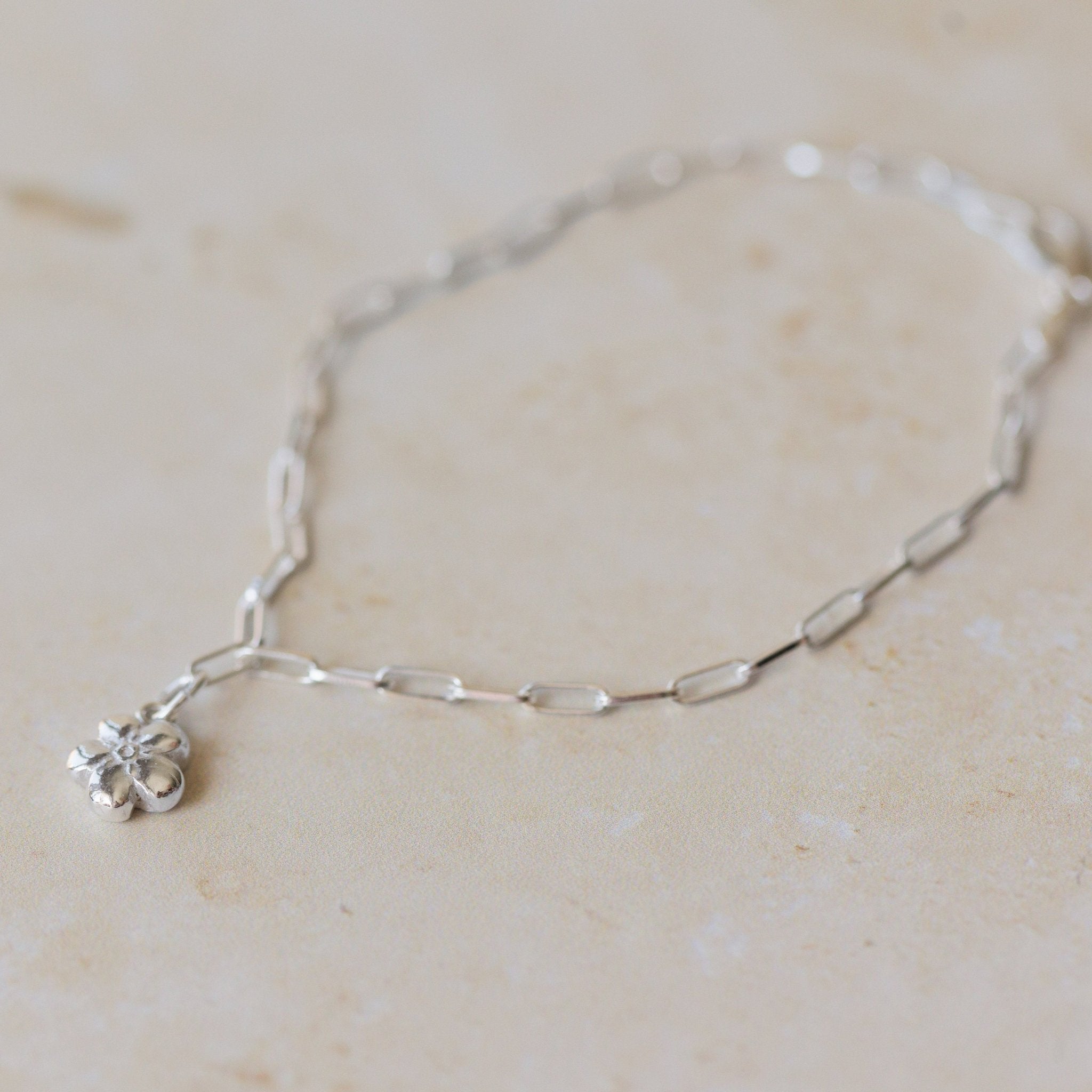 silver forget me not charm bracelet with paperclip chain styled flat on neutral background, delicate floral jewellery by Iris & Lolli