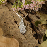 silver oak leaf charm bracelet resting on natural bark with flowers and leaves, handcrafted woodland-inspired jewellery by Iris & Lolli