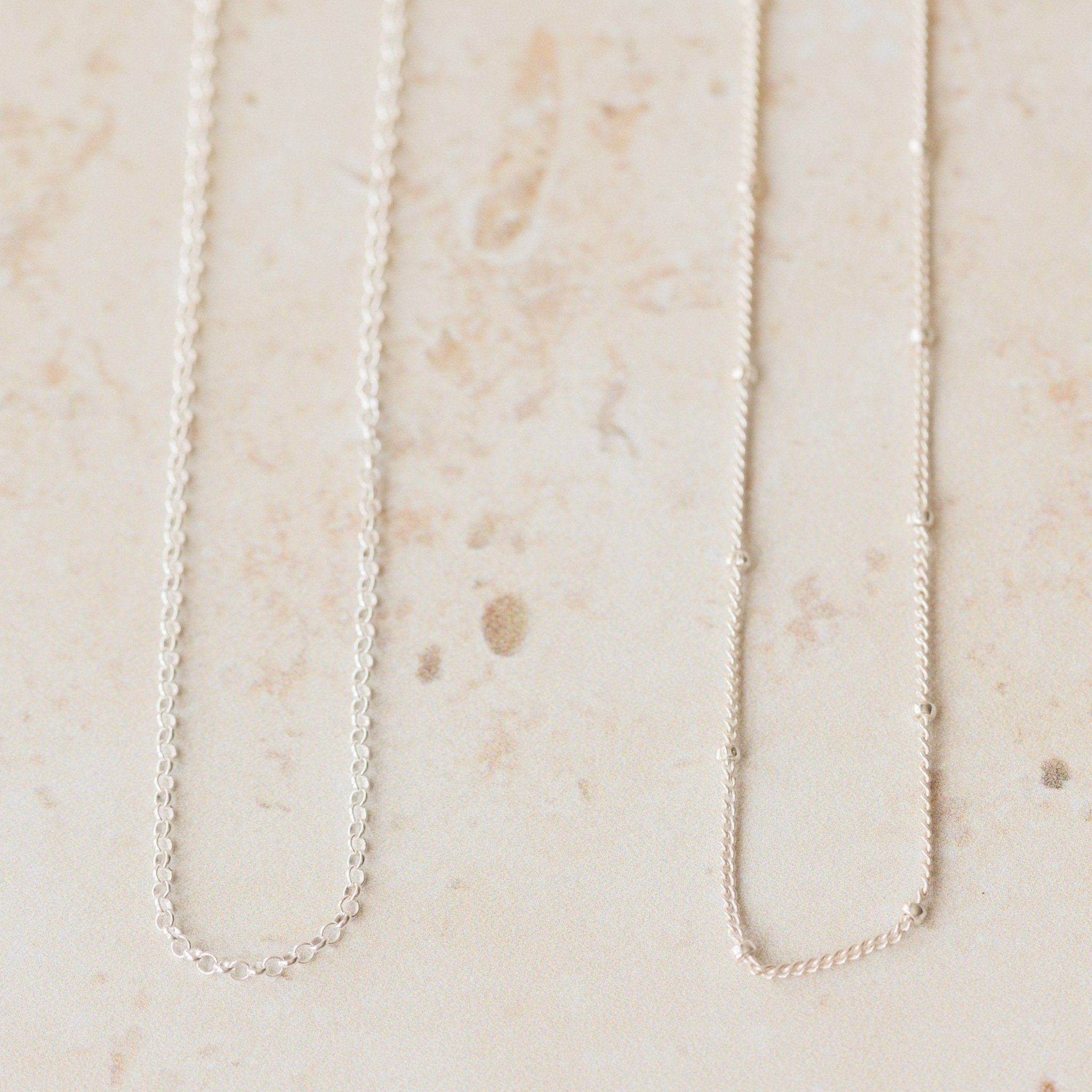 Two delicate silver chain necklaces, trace and satellite styles, shown side by side on a neutral background, perfect interchangeable chains for pendants.