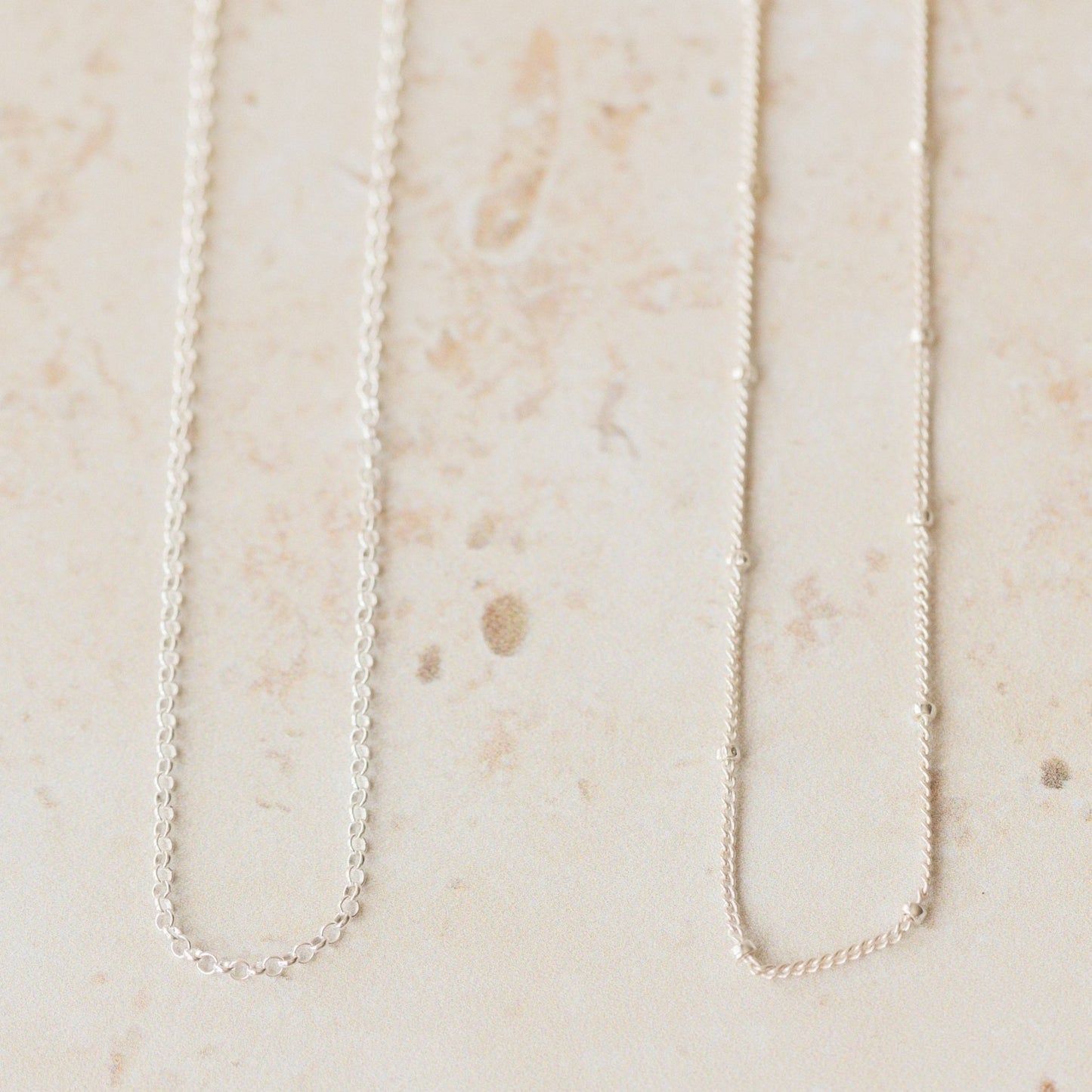 Two delicate silver chain necklaces, trace and satellite styles, shown side by side on a neutral background, perfect interchangeable chains for pendants.