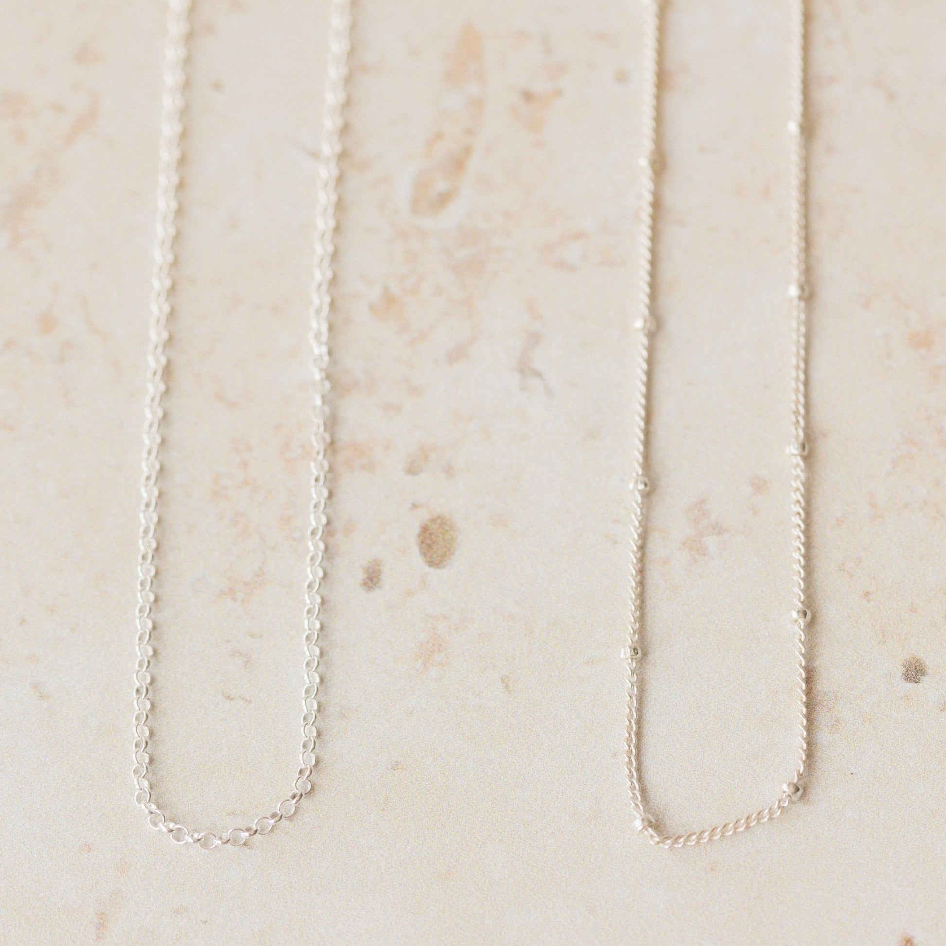 Two delicate silver chain necklaces, trace and satellite styles, shown side by side on a neutral background, perfect interchangeable chains for pendants.