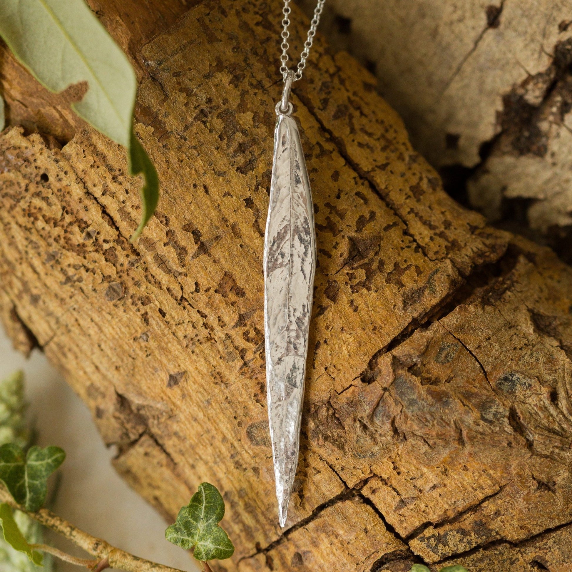 Handcrafted silver willow leaf necklace displayed on natural bark. Organic, textured recycled-silver pendant inspired by woodland leaves. Perfect nature jewellery gift.