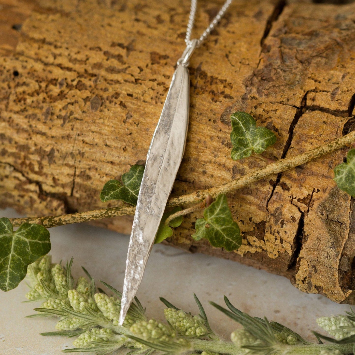 Handcrafted recycled-silver willow leaf pendant displayed on natural foliage. Textured, nature-inspired necklace perfect for woodland jewellery lovers.