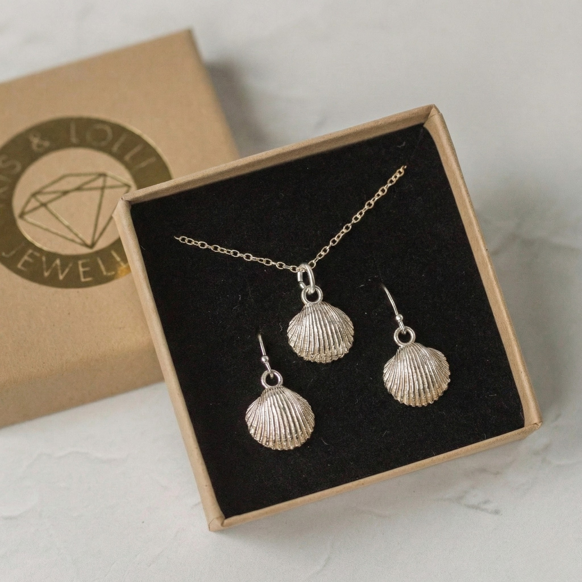 Handcrafted silver cockle shell earrings and matching necklace shown as a coastal jewellery set