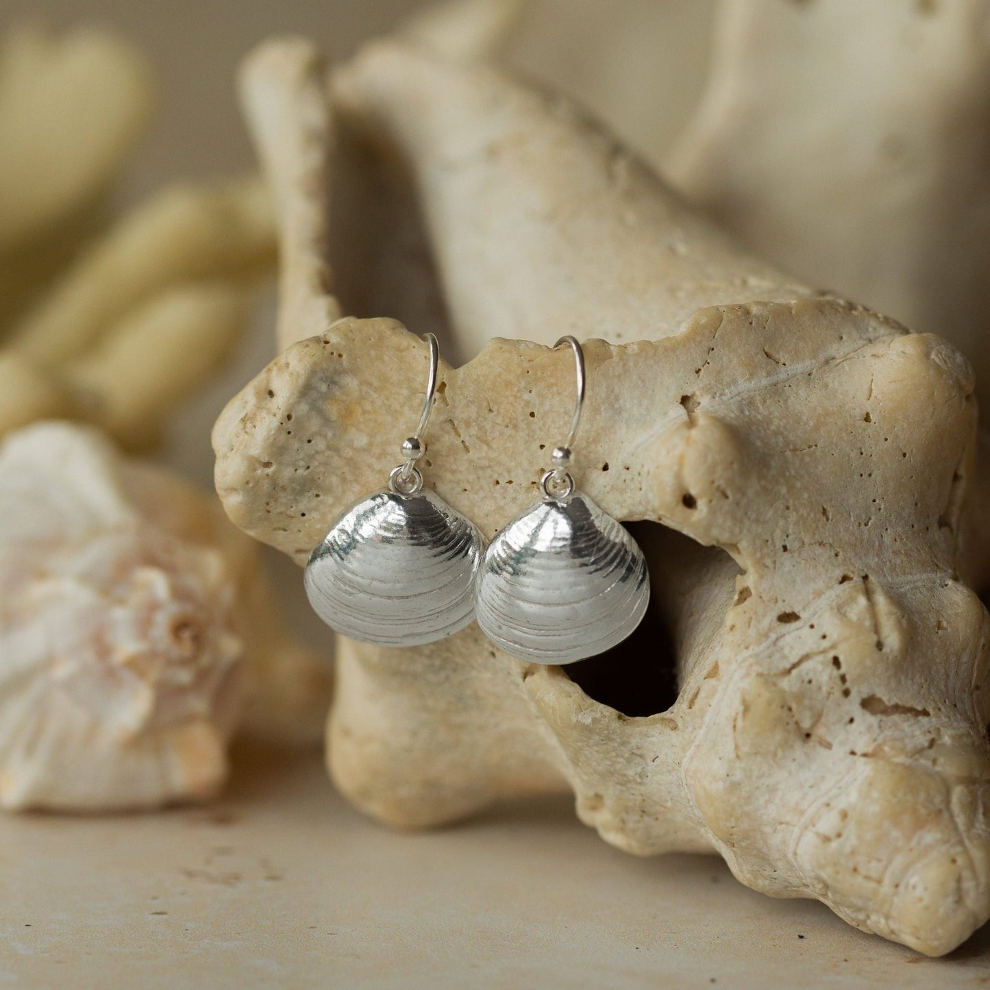 Handmade recycled silver Venus Clam earrings by Iris and Lolli displayed on natural coral and seashells, capturing their organic ocean texture and shimmering coastal elegance