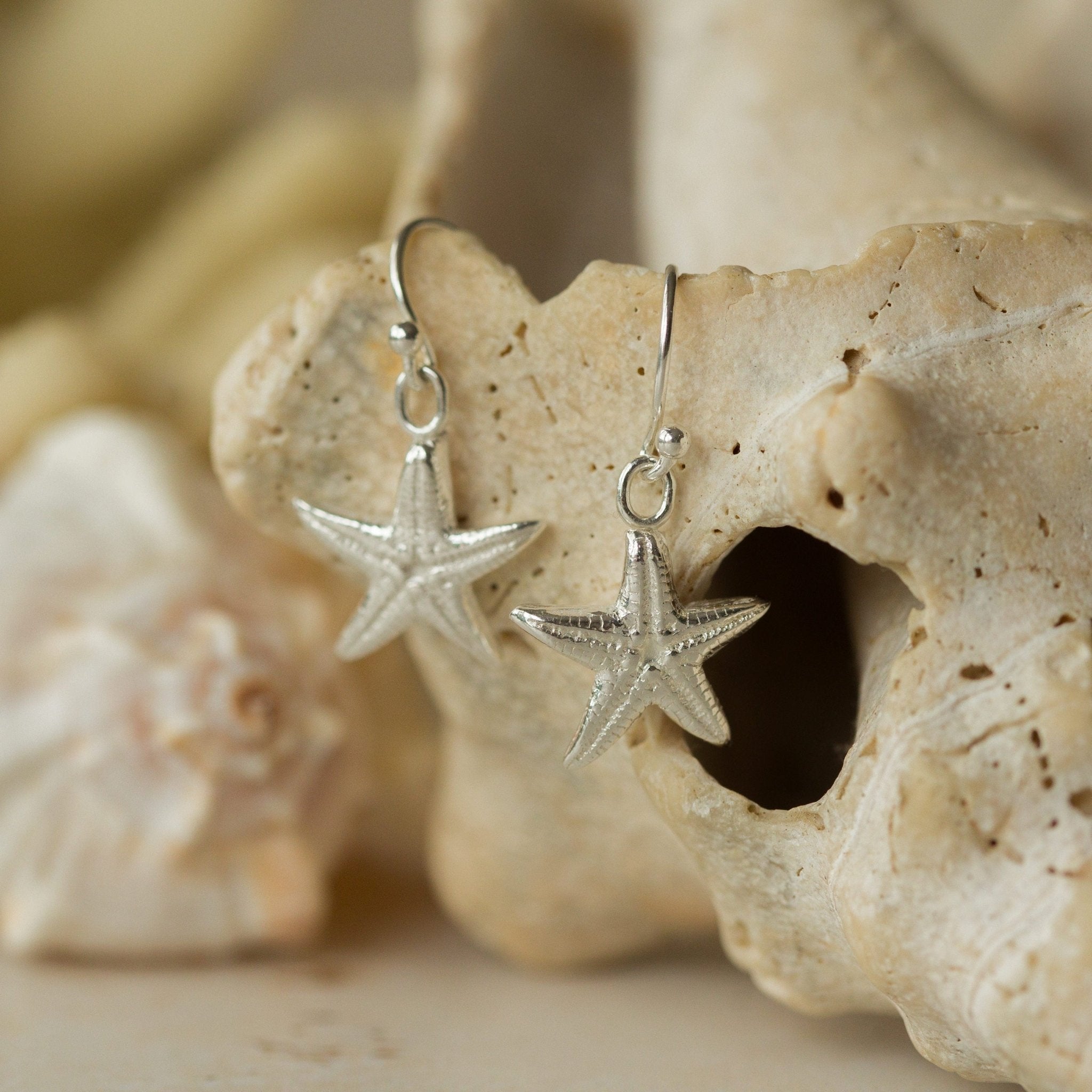 Handmade recycled silver Starfish earrings by Iris and Lolli resting on natural coral, featuring fine sea star detail and a soft ocean-inspired shine